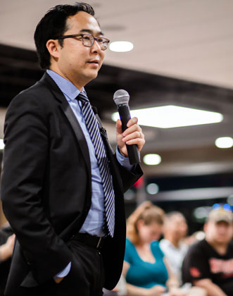 Andy Kim in a suit, holding a microphone
